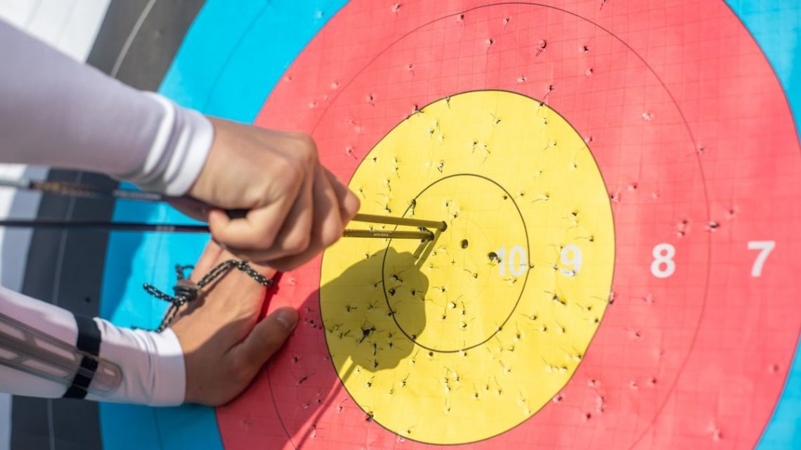 An archer retrieves arrows from a colorful archery target during a sunny day outdoors.
